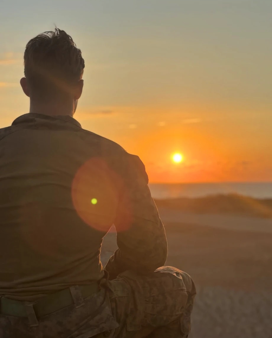 Landon Griffin in uniform, seen from behind, watching the sun set over the ocean
